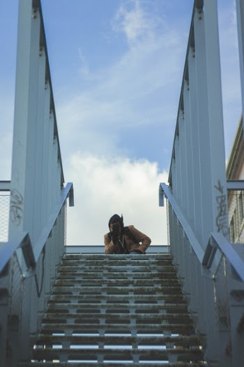 Person in Brown Coat on Bridge Under Cloudy Blue Sky