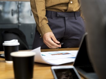 Person in Brown Dress Shirt and Black Bottoms Near Brown Wooden Desk