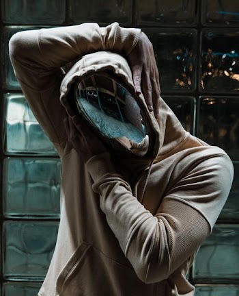 person in chrome mask and pullover hoodie behind clear glass wall