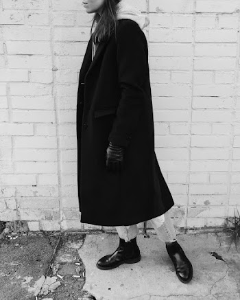 Person in Coat Standing Infornt of Brick Wall Greyscale Photography