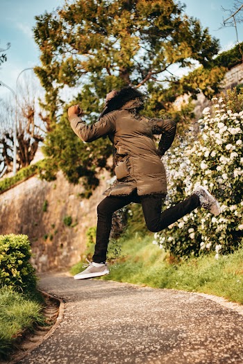 Person in Gray Coat Jumping on Gray Concrete Pathway
