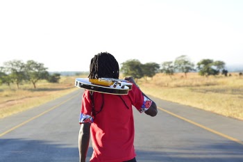 Person in Pink T Shirt Holding Brown Electric Guitar Walking on Blacktop Road during Daytime