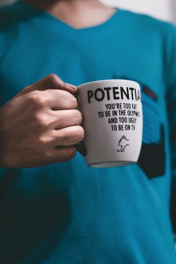 Person in Teal Shirt Holding White Ceramic Mug