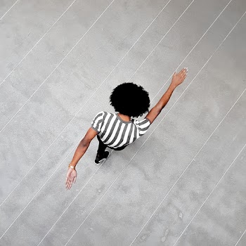 Person in White and Black Shirt Walks on Grey Pavement