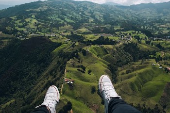 person in white sneakers facing aerial view of green mountain and houses