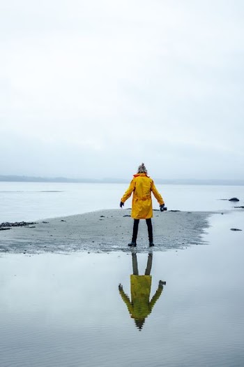 person in yellow coat on gray sand surrounded by water