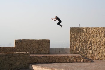 Person Jumping on Beige Concrete Wall