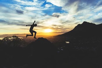 person jumping on hill during sunset