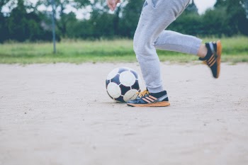 Person Kicking Soccer Ball on Gray Sand