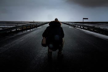 Person Kneeling on Concrete Pavement Wearing Parka Jacket