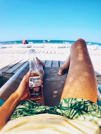 Person Laying On Lounge Chair Holding Corona Bottle