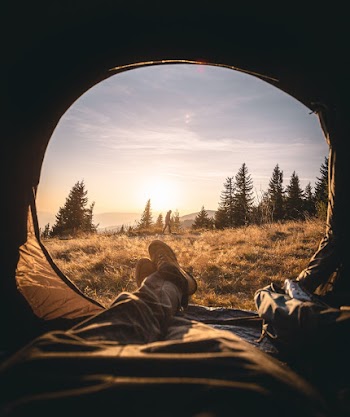 Person Lying Inside the Tent Through the Grass Field Under the Golden Hour