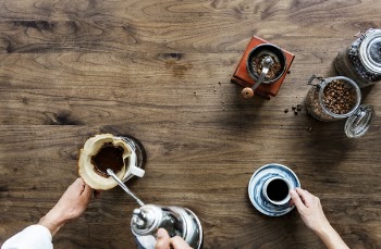 Person Making Coffee Beside Person Holding Cup of Coffee