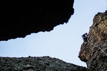person on blue shirt and black shorts climbing cliff