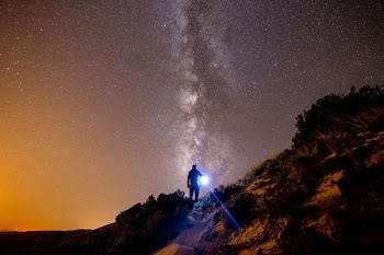 person on brown cliff under galaxy