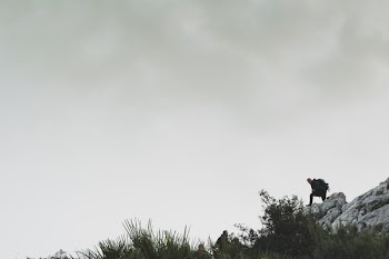 Person on Rocky Mountain Under White Cloudy Sky