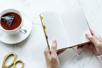 Person Opened a Book Near White Ceramic Cup Filled With Coffee