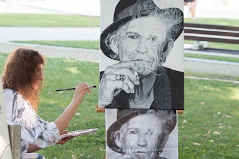 Person painting man's portrait from photograph outdoors