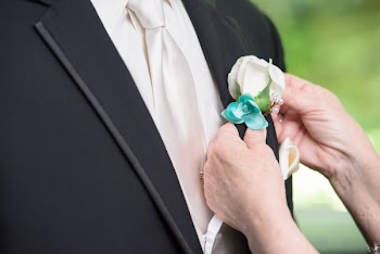 Person Putting White Rose Boutonniere On Man's Black Suit