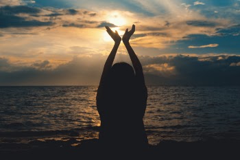 Person Raising Hands Near Sea at Sunset