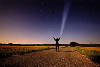 person raising his two hands while holding flashlight standing on road between grass during sunset