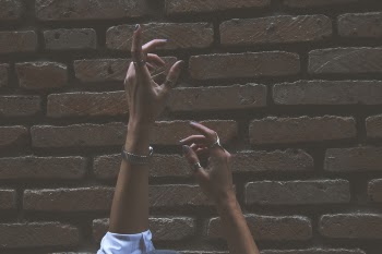 Person Raising Its Two Hand Beside Brown Brick Wall