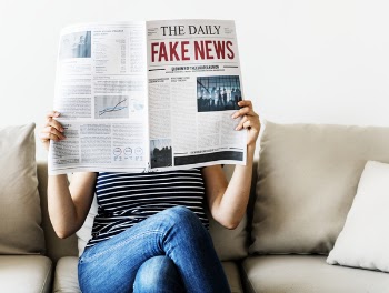 Person Reading the Daily Fake News Newspaper Sitting on Gray Couch