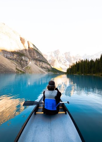 person riding kayak between mountain and trees