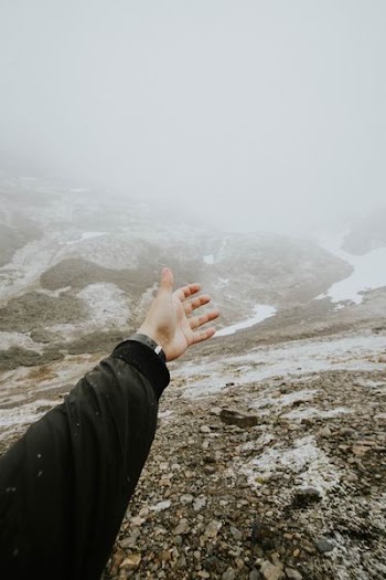 person rising their hand and facing at mountain
