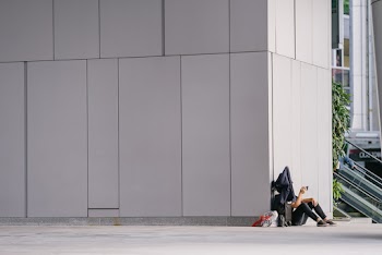Person Sitting down beside White Concrete Wall  