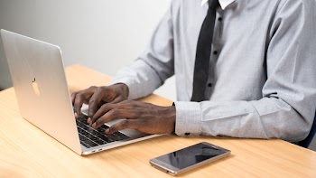 Person Sitting in Front of Table Using Laptop Beside Smartphone