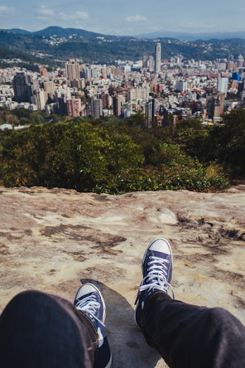 Person Sitting on Brown Rock Cliff While Overlooking on City Buildings