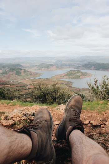 Person Sitting on Brown Soil    Overlooking Calm Body of Water