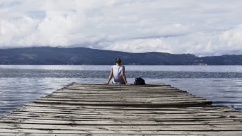 Person Sitting on Brown Wooden Dock Under Cloudy Blue Sky