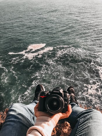 Person Sitting on Cliff While Holding Camera