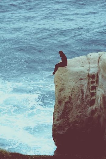 person sitting on edge of rock looking at sea