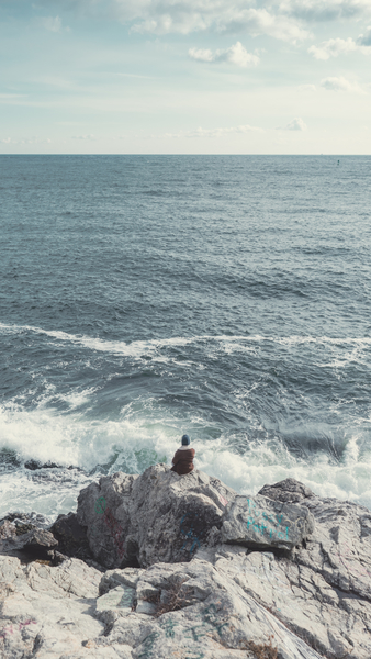 Person Sitting on Gray Rock Near Sea