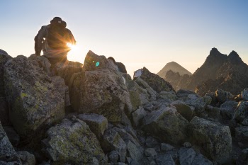 Person Sitting on Gray Rocks Under Clear Blue Sky