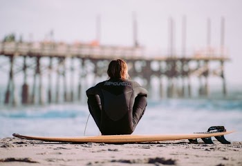person sitting on gray sand near body of water