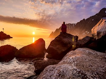Person Sitting on Rock Formation Beside Body of Water
