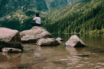 person sitting on rock formation facing mountains