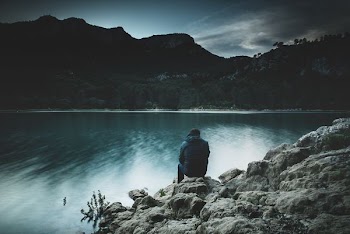 person sitting on rock near body of water