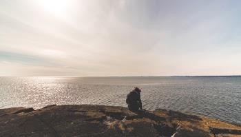 Person Sitting on Stone in Front of Sea Water