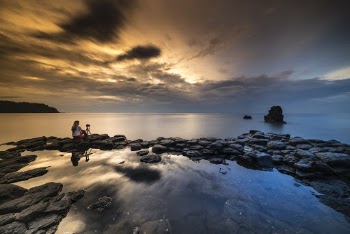 Person Sitting On Stone While Facing The Calm Sea During Sunset