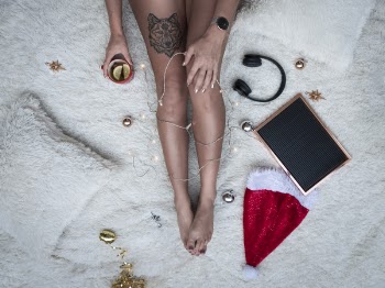 Person Sitting on White Fur Fabric Holding String Lights and Mug Beside Cordless Headphones