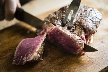 Person Slicing Meat On Cutting Board