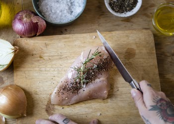 Person Slicing Raw Meat With Pepper on Chopping Board Beside Spices