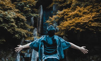 Person Spreading His Hands in Front of Gray Concrete Structure Surrounded by Brown and Green Leaf Trees