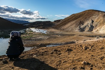 Person Squatting Front of Brown Mountain