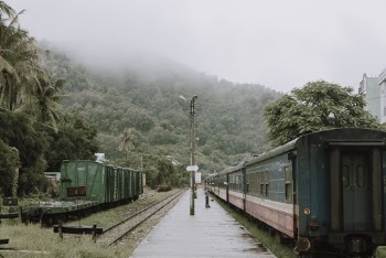 Person Standing  By An Old Train  In A Train Stop Close To A Mountain With Tick Vegetation  